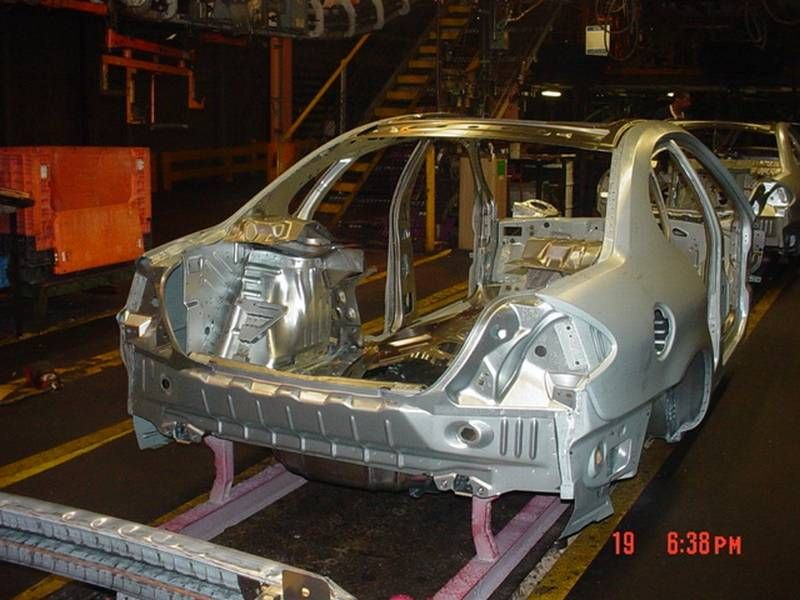 Car body shell on an assembly line, showing the unpainted metal frame. Another car body is visible behind it