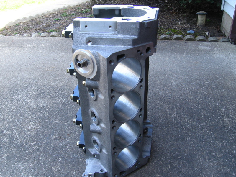 Machined V8 engine block standing on a driveway, honed bores and deck surface visible