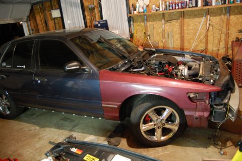 1985 Mercury Grand Marquis - A car is in a garage with its hood open, revealing the engine and front-end components.