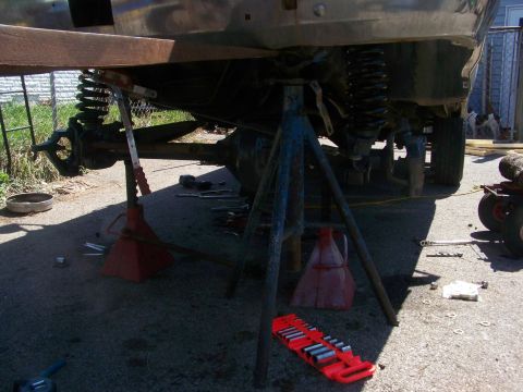 1989 Ford Bronco - The underside of a vehicle is supported by jack stands, revealing suspension and axle components during a repair or modification.