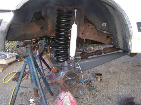 1989 Ford Bronco - The vehicle's front axle and suspension are disassembled, showing new shocks and springs being fitted.