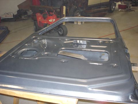 1979 Ford F-250 - A bare vehicle door is shown in a workshop setting, with other vehicles and equipment in the background.