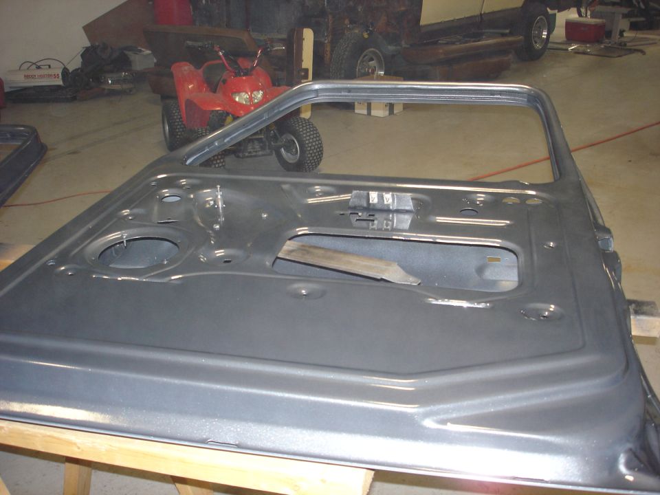 Gray vehicle door, stripped down, sitting on sawhorses. Red ATV and part of another vehicle in background