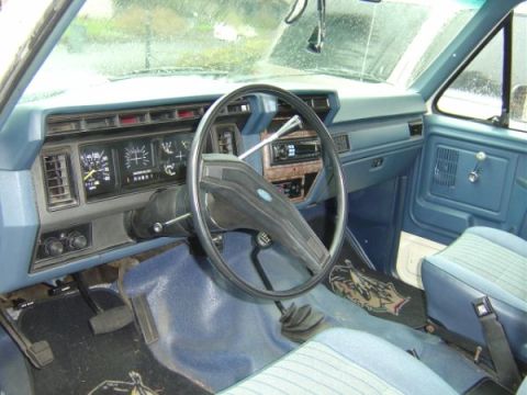 1985 Ford Bronco - The interior floor shows signs of rust and wear around a plastic grommet and wiring harness.