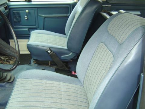 1985 Ford Bronco - The interior of a blue minivan is shown from the perspective of the rear seats, looking forward.