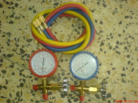 1998 Ford Crown Victoria - A Qing Xin A/C manifold gauge set laid out on a terrazzo tile floor, with the red high-side and blue low-side gauges on brass valve bodies…