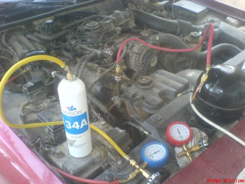1998 Ford Crown Victoria - A/C service setup staged in the dusty engine bay of a maroon car: a white "Season 134A" refrigerant can stands on the engine with a yellow…