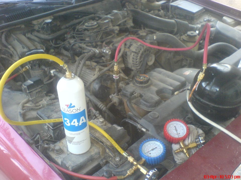 R134a can, manifold gauges and improvised vacuum pump set up in a dusty engine bay