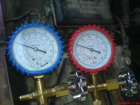 1998 Ford Crown Victoria - Close-up of a Qing Xin A/C manifold gauge set resting on components in an engine bay, with the blue low-side gauge on the left and the red…