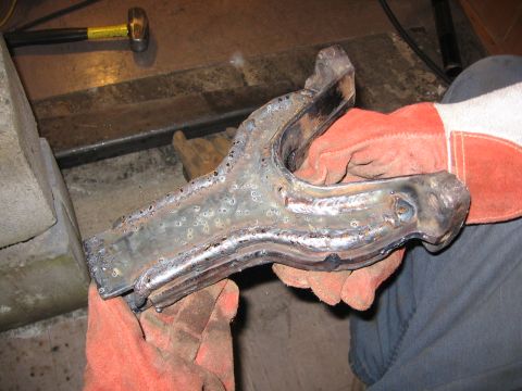 1989 Ford Bronco - A metal part, likely from a vehicle's suspension, is held by gloved hands after being welded.