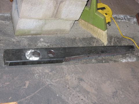1989 Ford Bronco - A metal component, possibly a frame piece, rests on a dusty concrete surface next to a broom and extension cord.