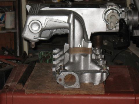1994 Ford Bronco - Intake manifold, likely for a V8 engine, sits on a wooden block in a workshop setting.