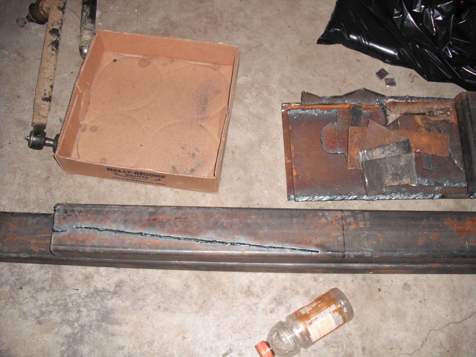 Metal tubing with a cut slot, a metal bracket, a cardboard box labeled KELLY MOORE PAINTS, and a plastic bottle on a concrete floor