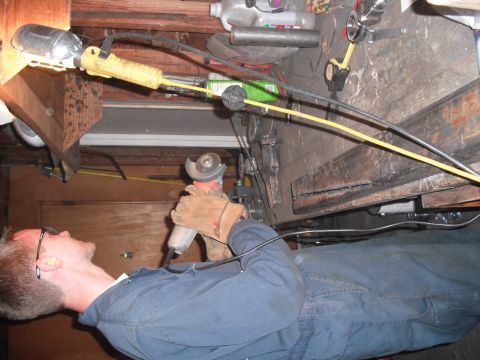 1991 Ford Bronco - A person wearing safety glasses and ear protection uses an angle grinder in a workshop setting.