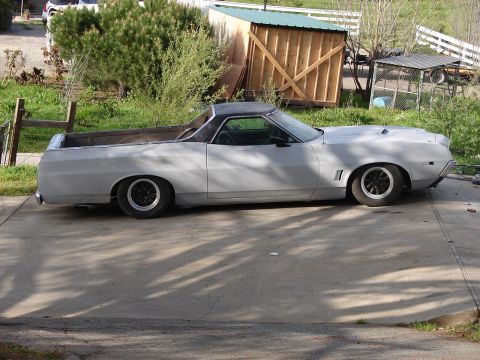 1973 Ford Ranchero - A light gray 1973 Ford Ranchero pickup truck is parked on a concrete driveway, showing its side profile and custom wheels.