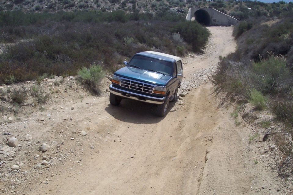 Teal Ford Bronco driving on a dirt road