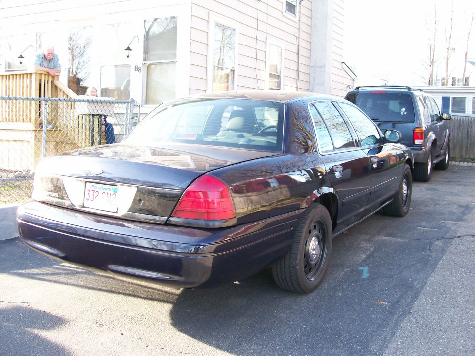 Dark blue 2007 Ford Crown Victoria sedan parked on asphalt, rear 3/4 view, with a dark SUV behind it