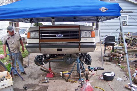 1989 Ford Bronco - A 1989 Ford Bronco's front end is lifted for axle swap work under a blue canopy.