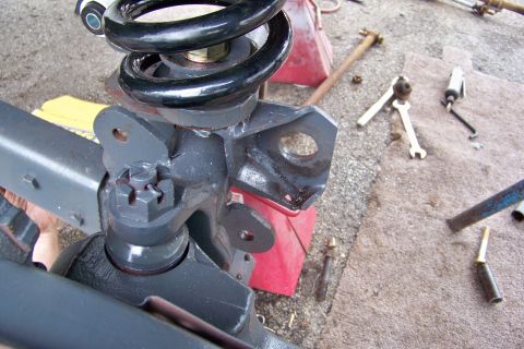 1989 Ford Bronco - A close-up view of a vehicle's suspension components, including a coil spring and mounting bracket, with tools scattered around.