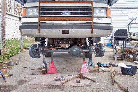 1989 Ford Bronco - Front axle of a 1989 Ford Bronco, lifted on jack stands for service, with a 4x4 badge on the grille.
