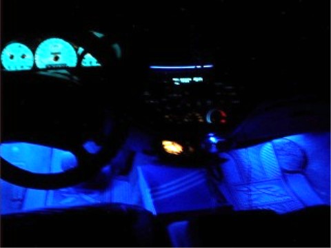 1997 Ford Taurus - Dim night interior shot showing a steering wheel, illuminated gauge cluster and blue LED footwell lighting on the floor.