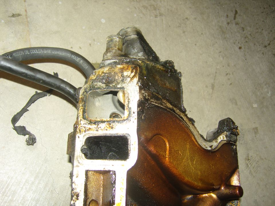 worn engine intake manifold part with black hose attached, text on hose reads 'TRANSMISSION OIL COOLER 3/4"'