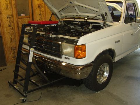 2007 Ford Mustang - White Ford F-150 truck with hood open, undergoing repairs with a topside creeper tool.