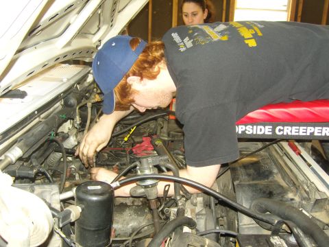 2007 Ford Mustang - A person works on the engine of a vehicle, with another person observing in the background.