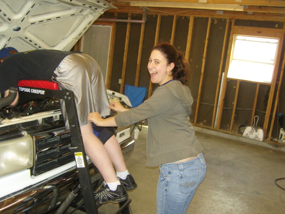 Person on creeper under hood of white 1987 Ford F-150, front grille visible