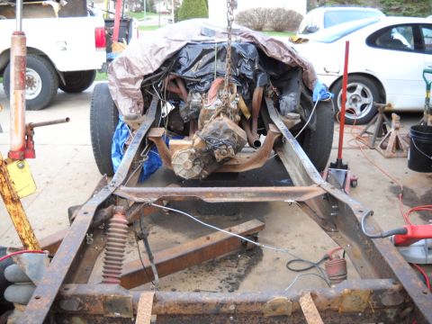 1954 Ford F-100 - Engine and chassis assembly suspended for work, with other vehicles visible in the background.