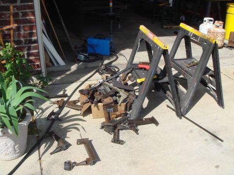 1992 Ford Bronco - A collection of metal parts and welding equipment are laid out on a concrete surface, with sawhorses in the background.