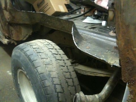 1993 Ford Bronco - Close-up of a vehicle's rear wheel well, showing rust and damage to the body panel and suspension.