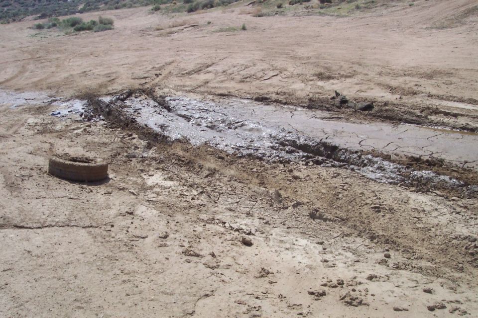 Muddy track with a tire and cracked earth, Supermotors.net logo visible