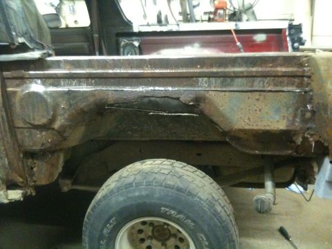 1993 Ford Bronco - Close-up of severe rust damage on a vehicle's body panel, with a tire in the foreground.