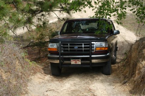 1996 Ford Bronco - This 1996 Ford Bronco is driving on a sandy, off-road path surrounded by trees.