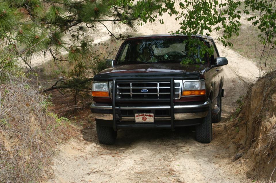 Dark Ford SUV with grille guard on a sandy wooded trail, front view