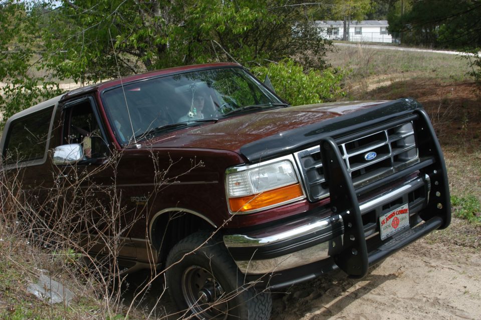Maroon Ford Bronco SUV, 3/4 front view, with black brush guard in brushy dirt setting