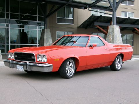 1973 Ford Ranchero - Three-quarter front view of a lowered orange-red Ford Ranchero coupe-utility on polished five-spoke wheels with low-profile tires, parked u…