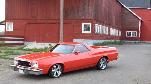 1973 Ford Ranchero - Red Ford Ranchero coupe utility posed in front of a weathered red barn, shot from the front three-quarter driver's side. It rides on polish…