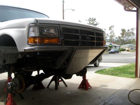 1996 Ford Bronco - The front end of a white Ford truck is elevated on jack stands, revealing its grille and a custom bumper.