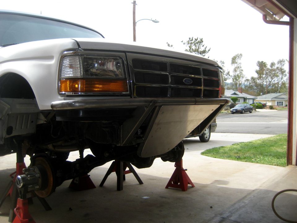 Front of a white Ford truck on jack stands, showing the grille and custom bumper