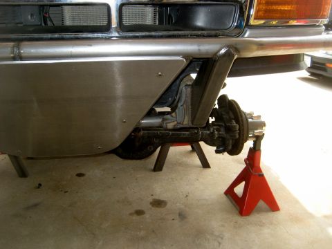 1996 Ford Bronco - Close-up view of a custom metal front bumper and suspension system, with the vehicle supported by red jack stands.