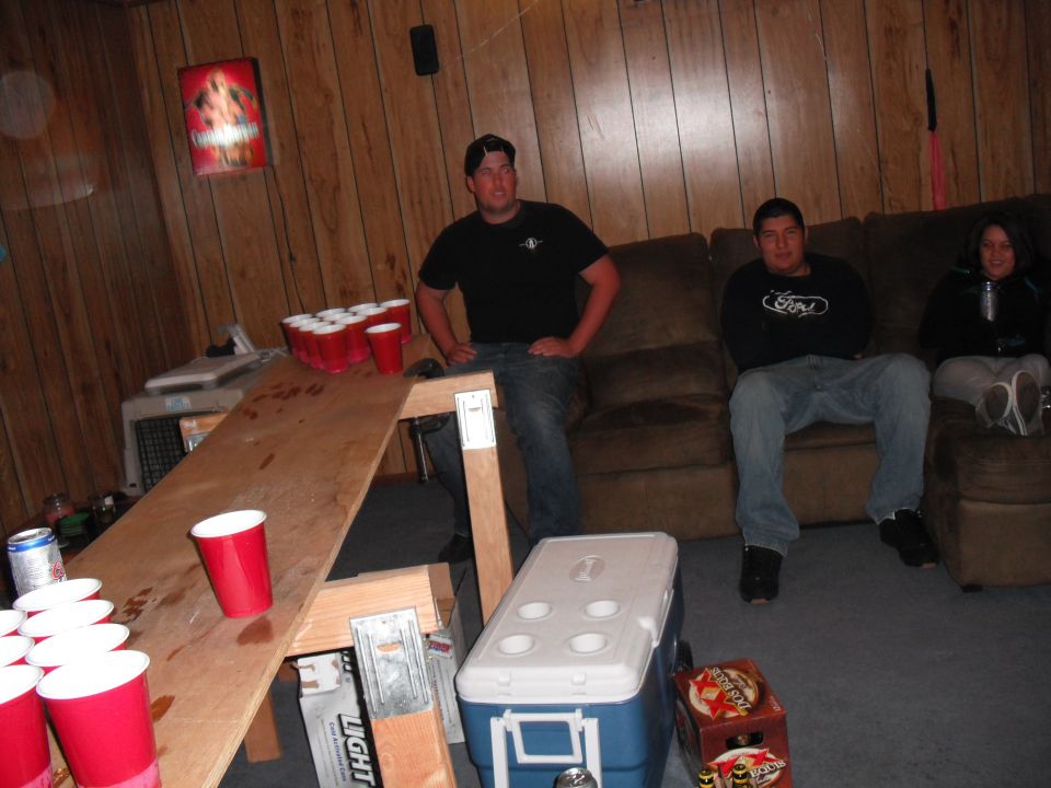 People sitting on a couch in a room with a beer pong table and red cups