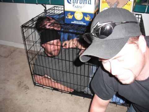 1991 Ford Bronco - Two men are confined within a large wire dog crate, with a third person partially visible in the foreground.