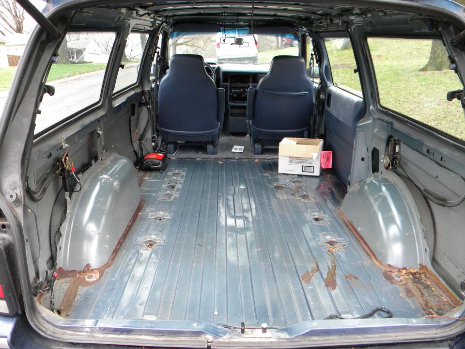 Minivan interior stripped to bare metal floor, rear seats and carpet removed, blue front buckets