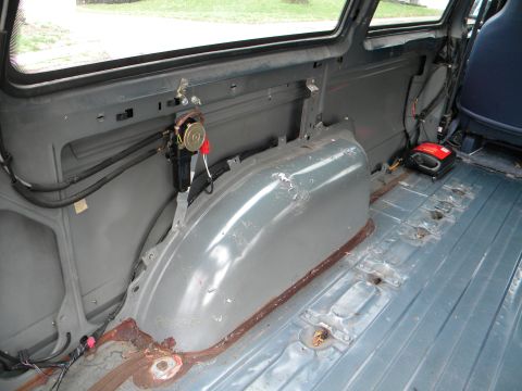1993 Dodge Grand Caravan - Rear interior of a van, seats removed, showing bare metal floor and wheel well.