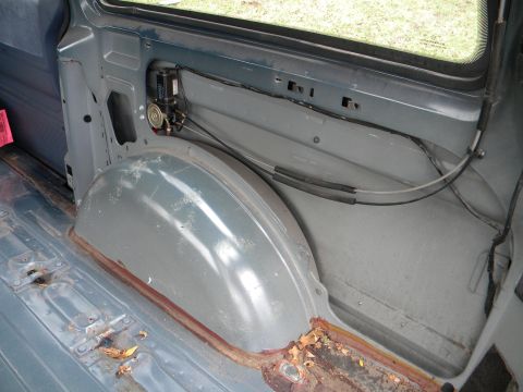 1993 Dodge Grand Caravan - The rear interior of a van shows the wheel well and some signs of rust and wear.
