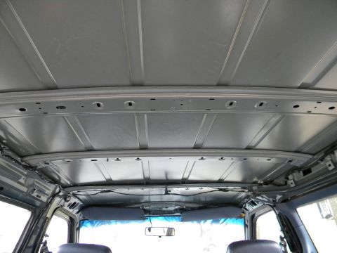 1993 Dodge Grand Caravan - The interior ceiling of a vehicle shows exposed metal framework and wiring, with sun visors partially visible.