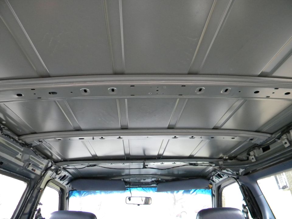 Vehicle interior ceiling with exposed metal ribs and wiring. Sun visors visible