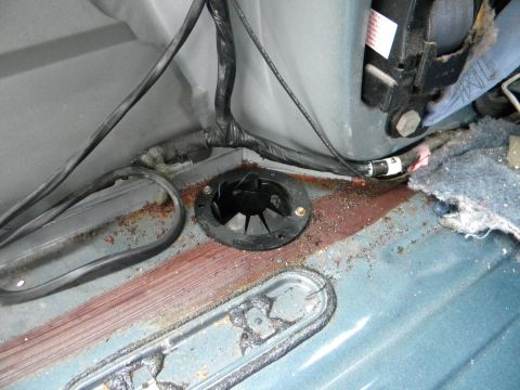1993 Dodge Grand Caravan - The interior floor of a vehicle shows signs of rust and exposed wiring around a black plastic grommet.